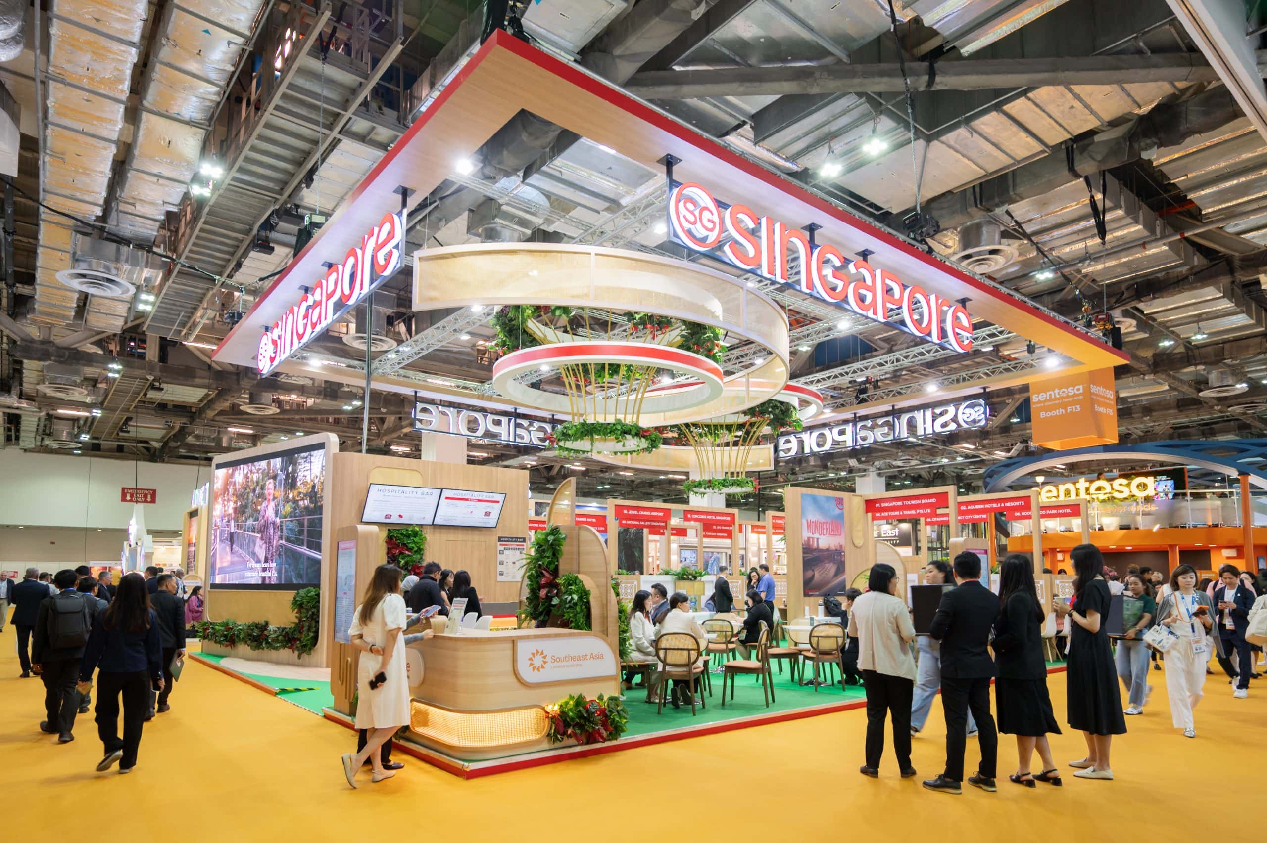 Singapore Tourism Board pavilion at ITB Asia travel trade show, featuring a large branded exhibition booth with greenery, meeting tables, and industry professionals networking on the show floor.
