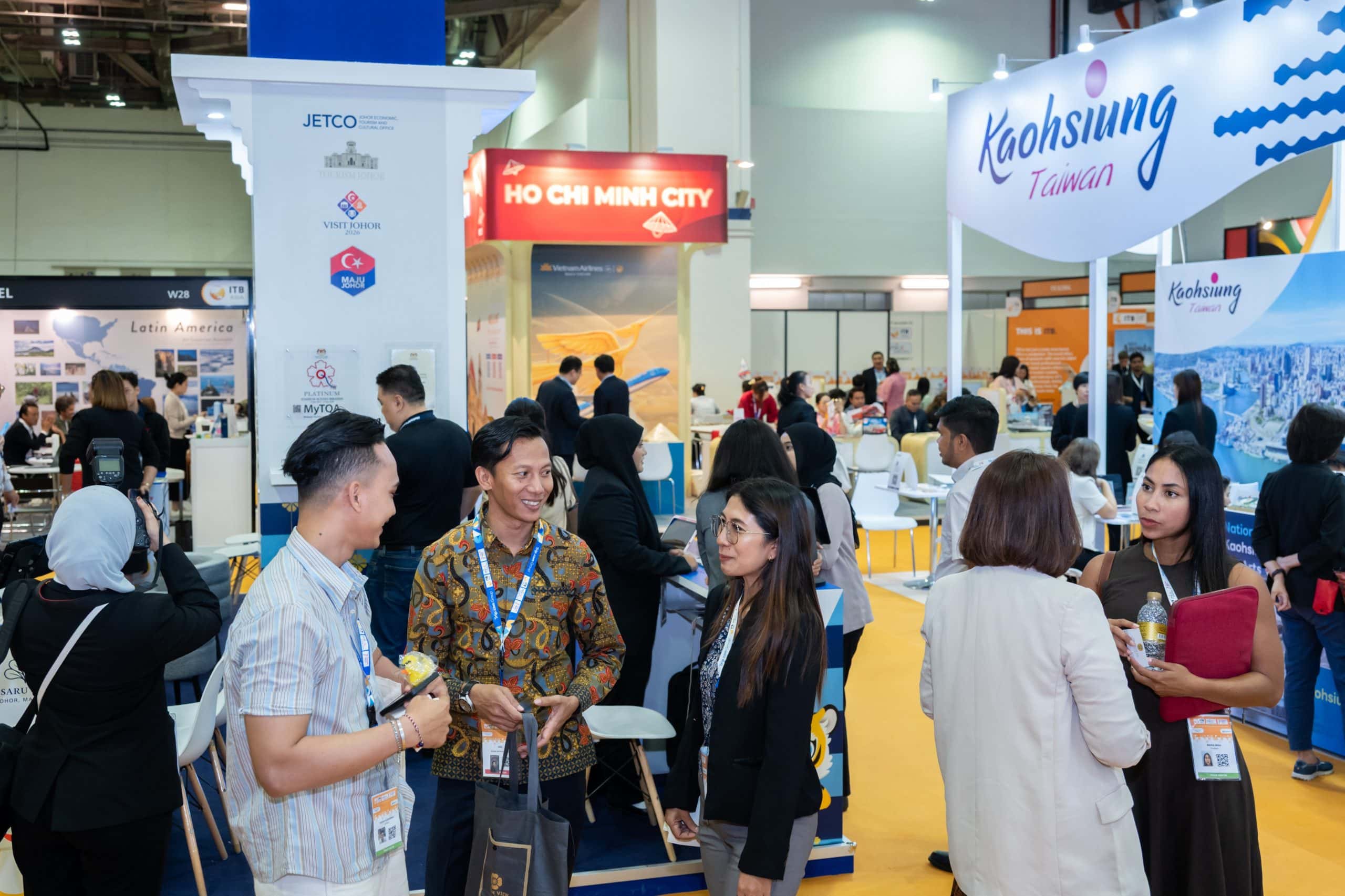 Travel industry professionals networking on the exhibition floor at ITB Asia 2025, with booths for Ho Chi Minh City, Kaohsiung Taiwan, Visit Johor, and Vietnam Airlines visible in the background.